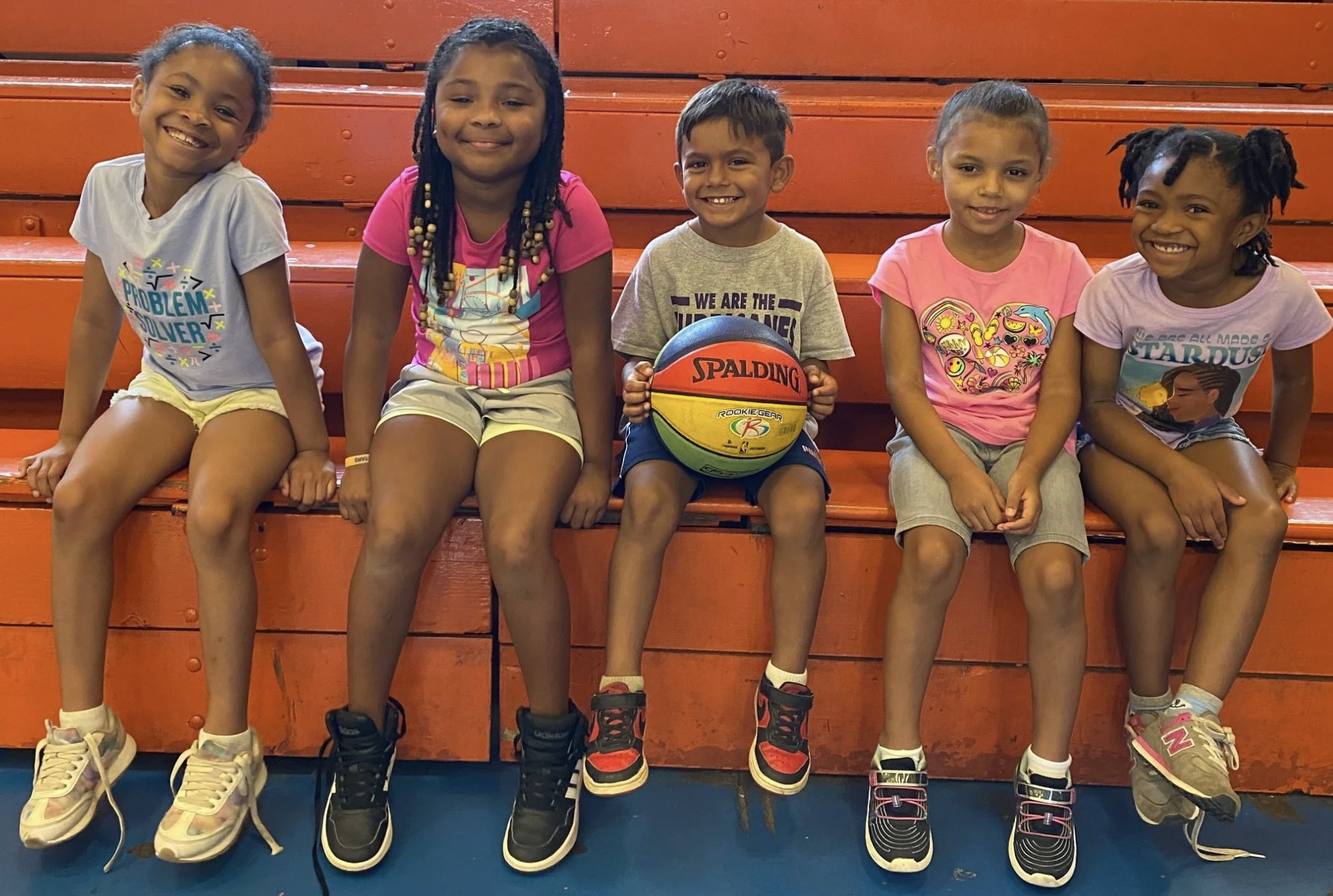 Five ELW campers on bleachers holding a basketball